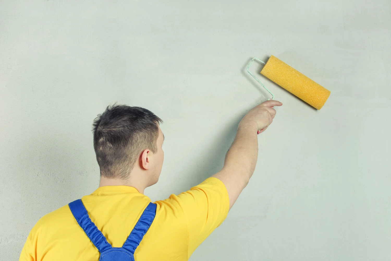 The repairman treats the wall with a primer using a roller. Light photo on the background of a gray wall.